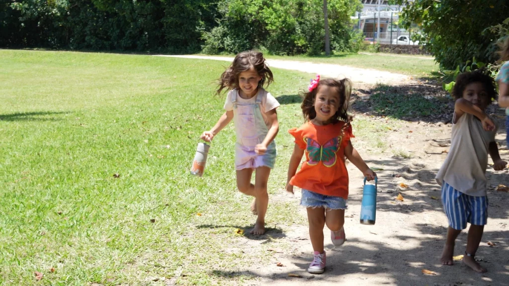 Três crianças correndo e brincando, levando as garrafas infantis com elas