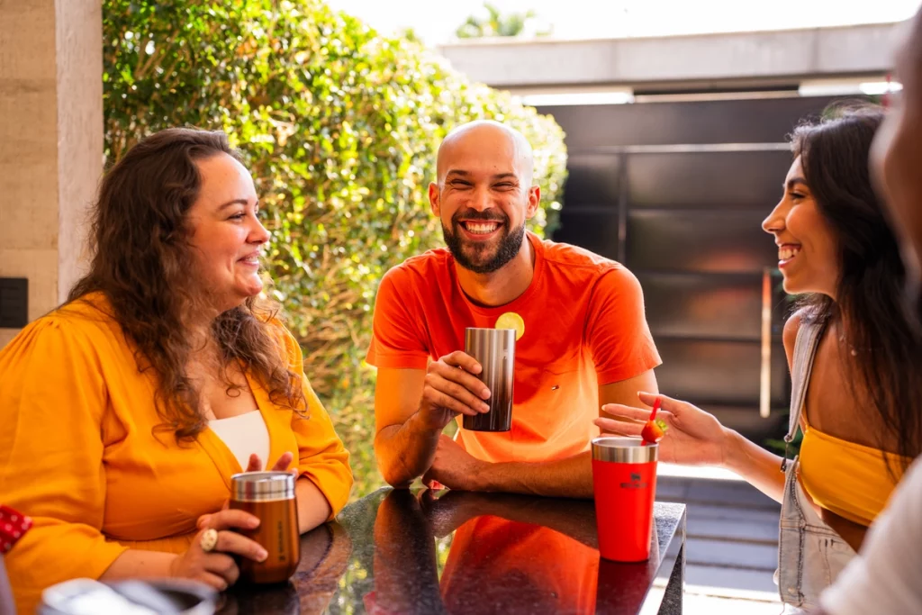 Quatro pessoas sentadas em volta de uma mesa, todos rindo e conversando enquanto aproveitam receitas de Festa Junina