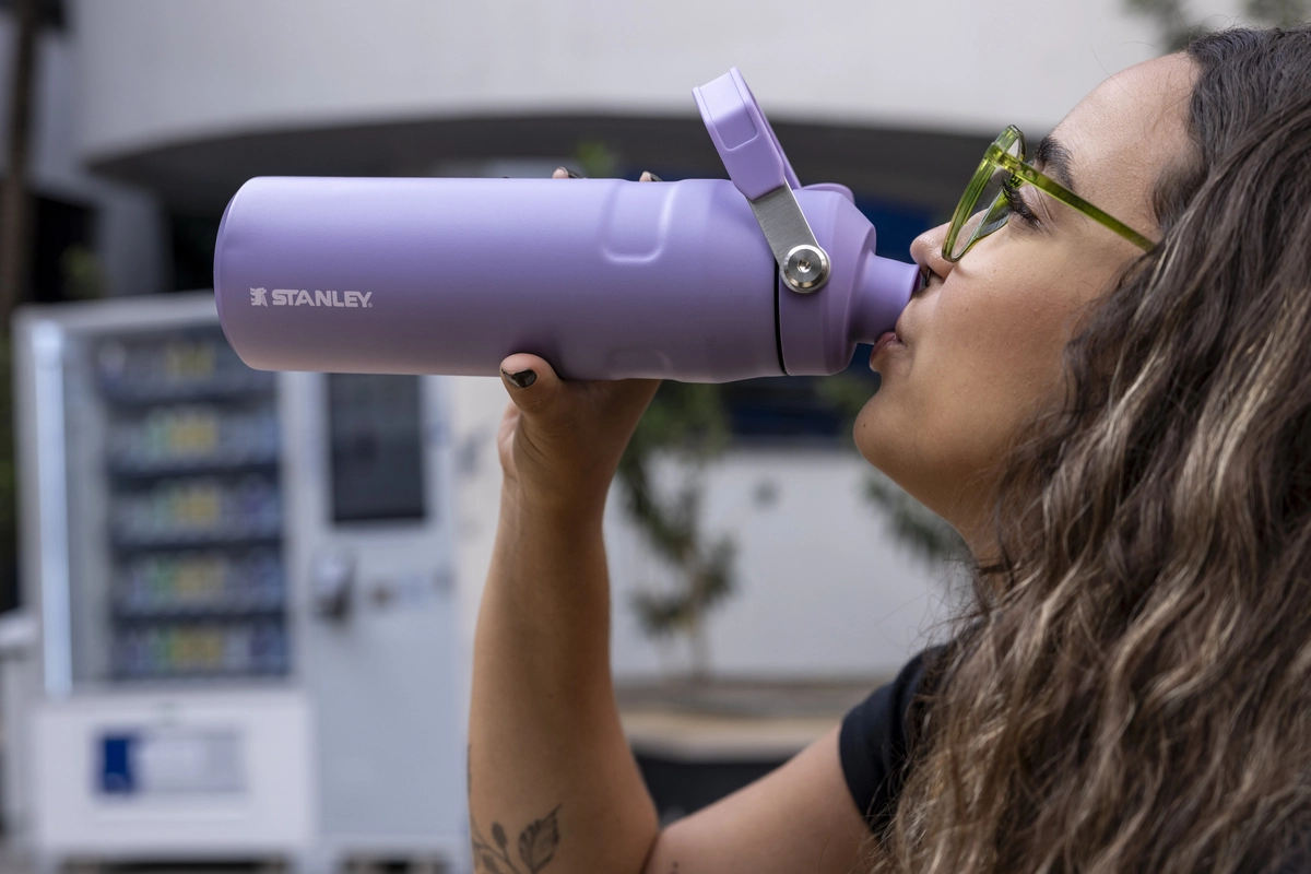 Uma mulher segurando uma garrafa térmica Stanley e usando ela para beber água.