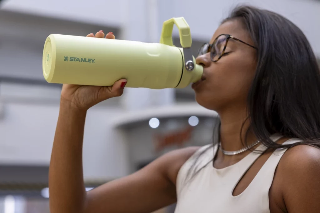 Uma mulher vista de lado, bebendo na sua garrafa Stanley ao saber se pode colocar refrigerante na garrafa Stanley