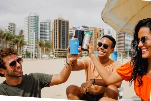 Três pessoas brindando com o Stanley Can Cooler na praia